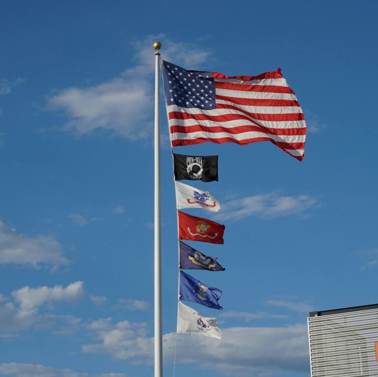 American flag and military service flags waving under a clear blue sky.